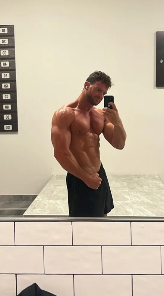 Zach’s personal progress at 12 months, in a gym mirror photo wearing black shorts